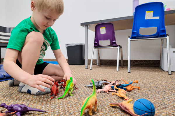 child-sitting-on-carpet-while-playing-with-plastic-dinosaurs-occupational-therapy-for-children-in-southern-oregon-explore-engage-enjoy-pediatric-therapy-clinic
